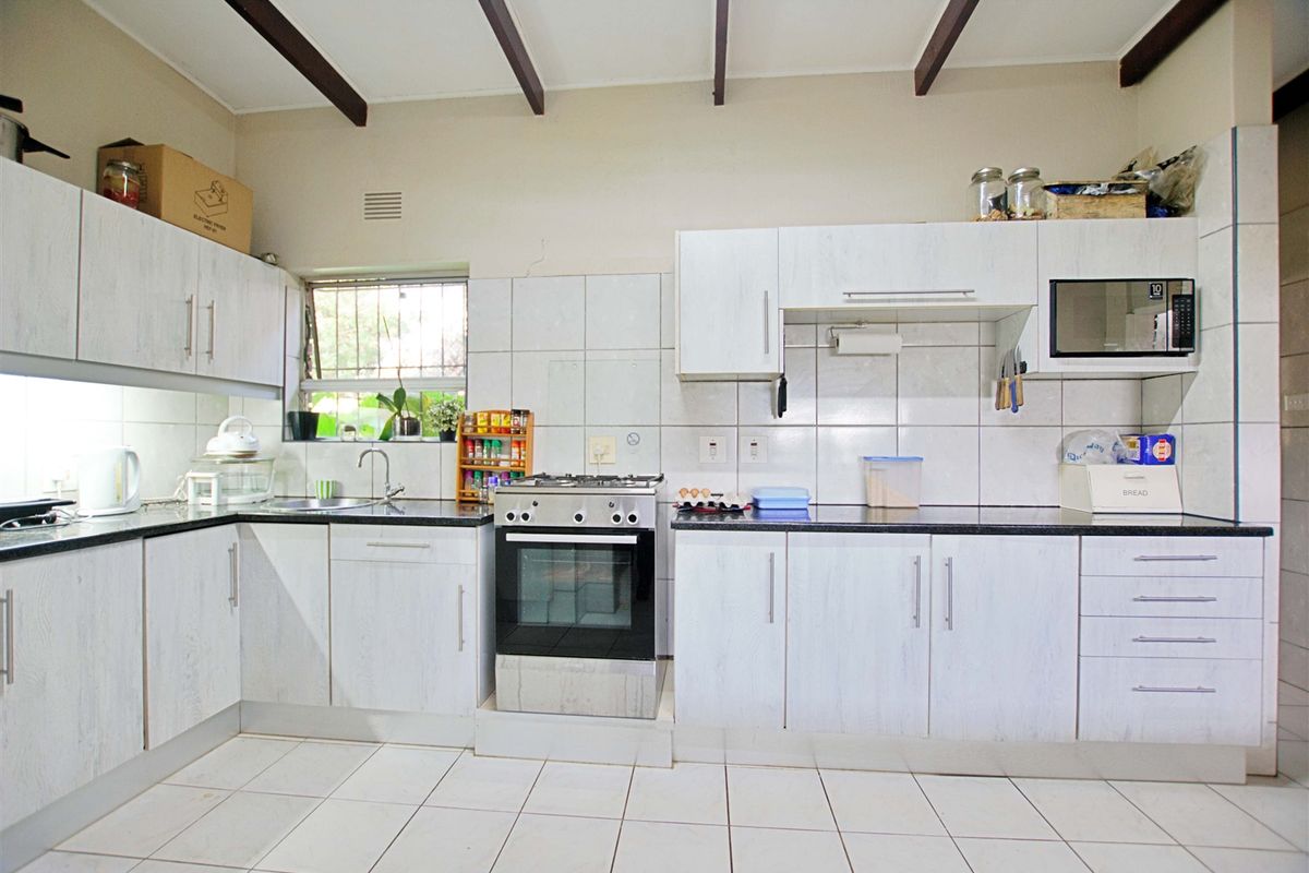 Functional kitchen featuring white cabinetry, dark countertops, tiled backsplash, and exposed ceiling beams, providing a practical workspace with integrated appliances.