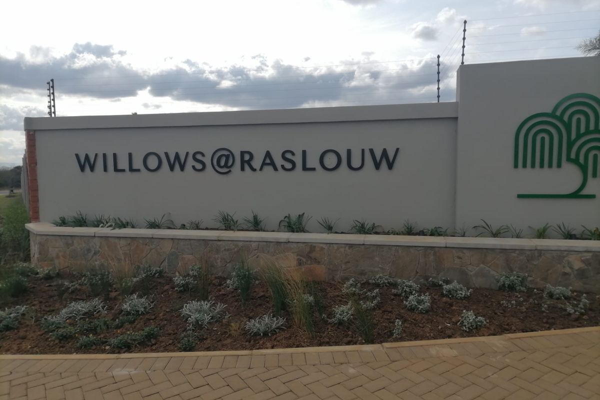 Entrance signage and boundary wall for Willows at Raslouw residential estate, featuring stone cladding, electric fencing, and manicured garden beds.