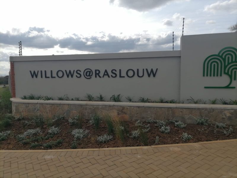 Entrance signage and boundary wall for Willows at Raslouw residential estate, featuring stone cladding, electric fencing, and manicured garden beds.