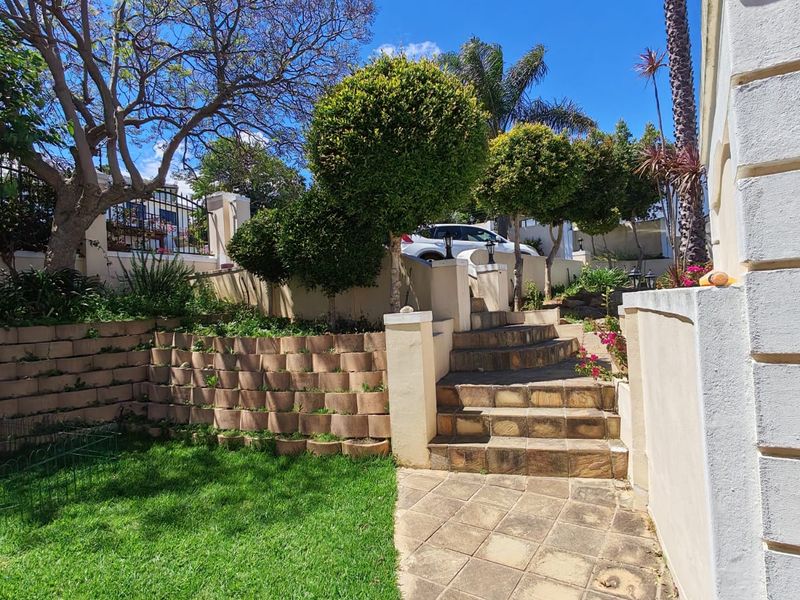 A landscaped garden area featuring a stone staircase, paved walkway, and tiered retaining walls leading to an elevated outdoor space.