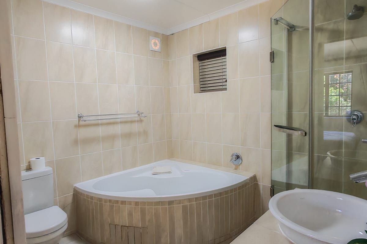 A functional bathroom featuring a corner bathtub, separate glass shower enclosure, vanity basin, and toilet with neutral wall and floor tiling.