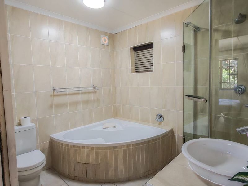 A functional bathroom featuring a corner bathtub, separate glass shower enclosure, vanity basin, and toilet with neutral wall and floor tiling.