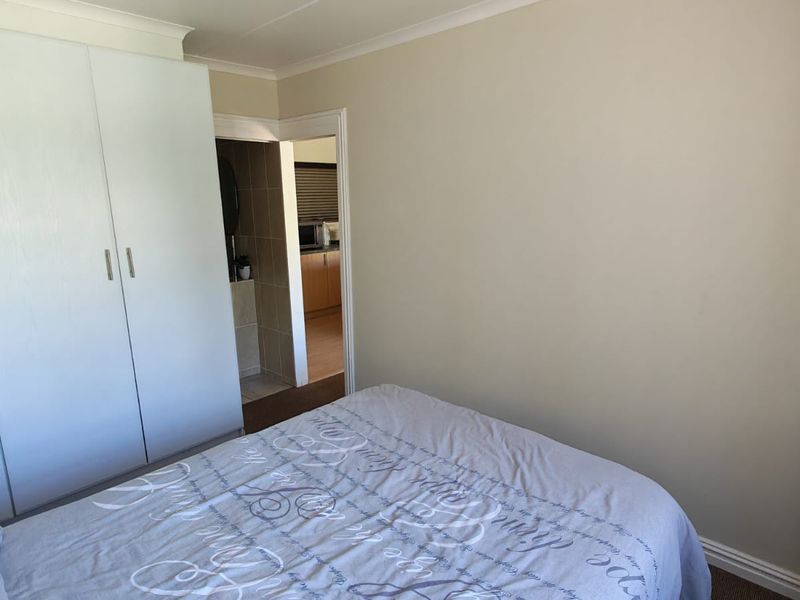 A bedroom featuring built-in cupboards and neutral wall finishes, with a view through to an adjacent room.