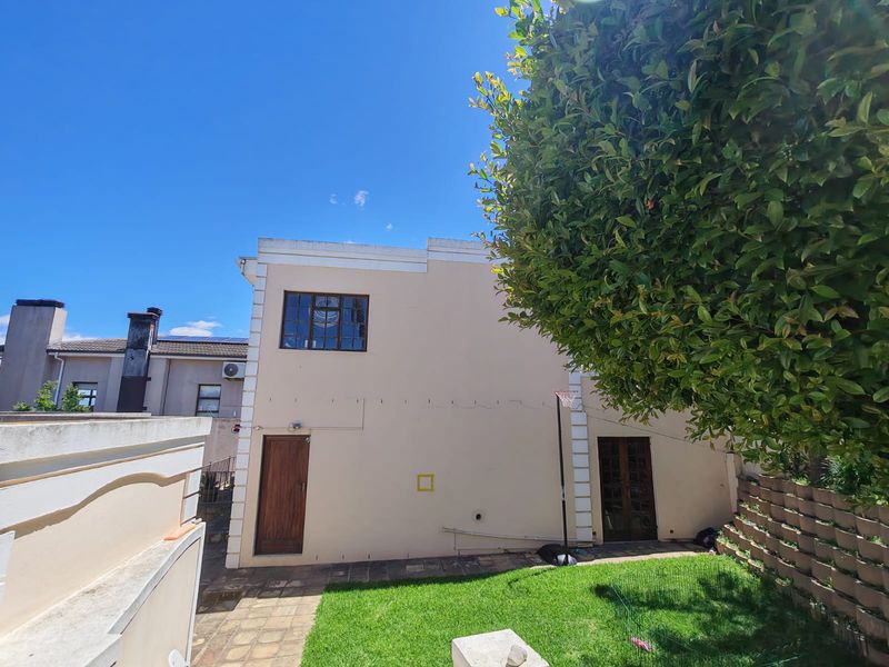 Rear exterior view of the townhouse featuring a paved patio area, small lawn, retaining wall, and access through timber doors.