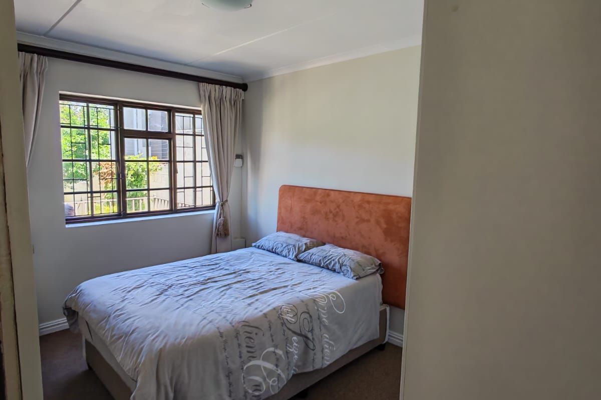 A standard bedroom featuring carpeted flooring, a window with security bars, and a ceiling light fixture.