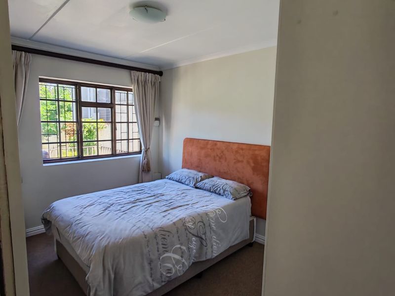 A standard bedroom featuring carpeted flooring, a window with security bars, and a ceiling light fixture.