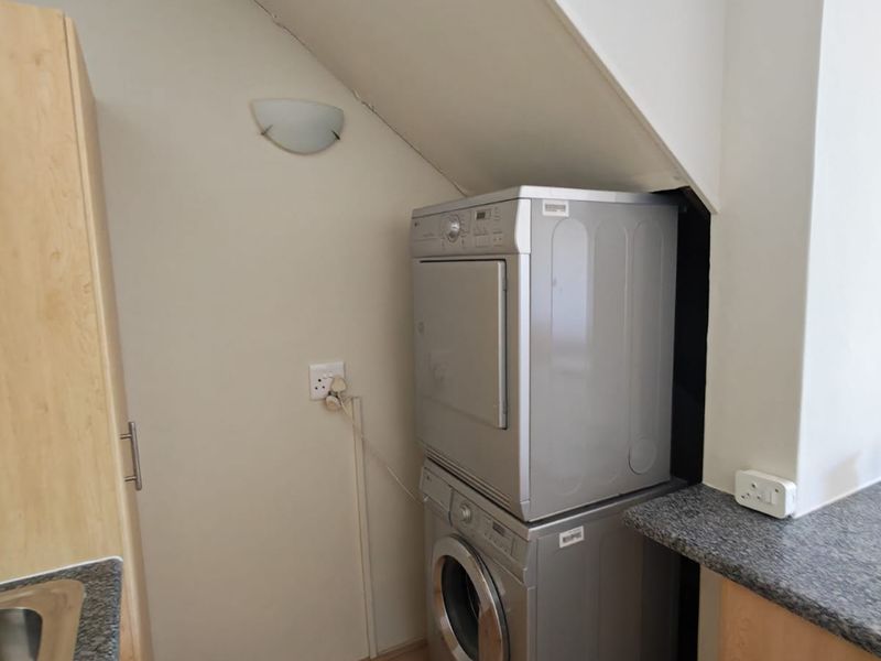 A compact laundry area tucked under the staircase, featuring laminate flooring, granite countertops, and built-in cabinetry for efficient utility space usage.