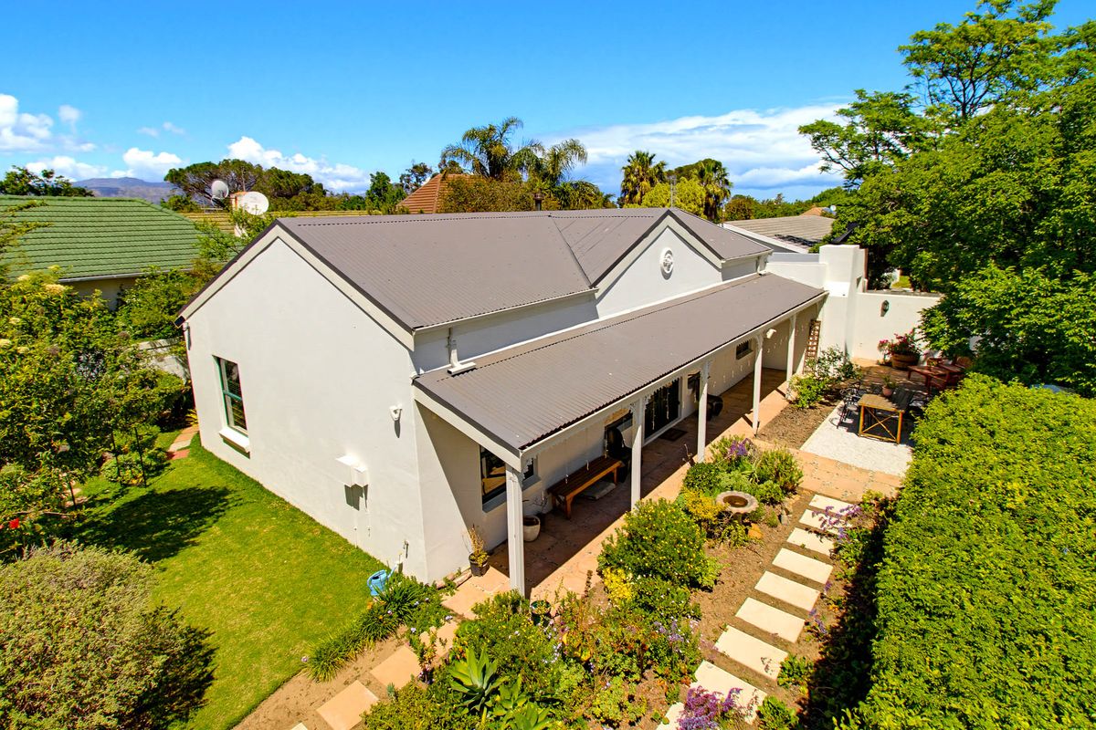 Aerial view of the rear elevation featuring a well-maintained garden, paved pathway, and a covered patio area with a corrugated metal roof.