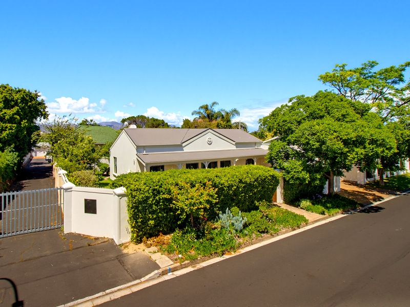 A well-maintained single-story house featuring a metal roof, a covered front veranda, and a secure perimeter wall with a gated driveway entrance.