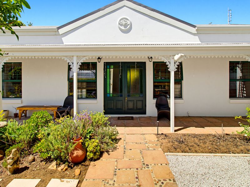Charming front facade featuring a covered veranda with decorative fretwork, stone paving, and a classic double-door entrance.
