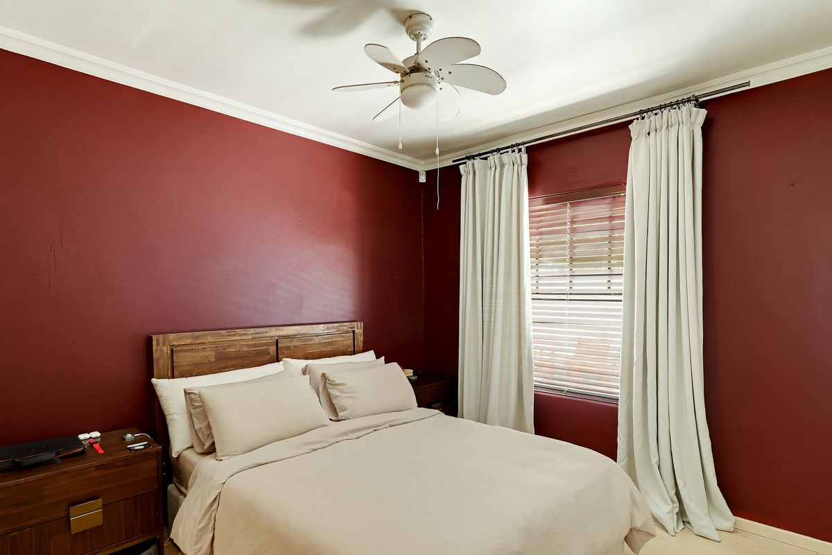 A bedroom featuring deep red walls, crown molding, a ceiling fan, and window blinds, offering a cozy space ready for personalization.