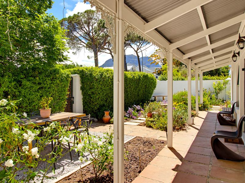 A charming covered patio featuring terracotta tiling, decorative wrought iron posts, and direct access to a landscaped garden with mountain views.
