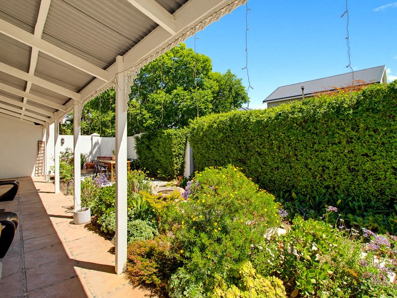 A covered patio area featuring tiled flooring, timber support posts with decorative detailing, and direct access to a well-maintained garden.
