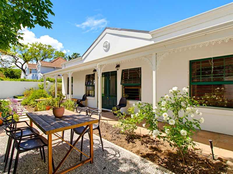 A charming rear exterior view featuring a covered patio with decorative wrought iron detailing, overlooking a well-maintained garden and gravel seating area.