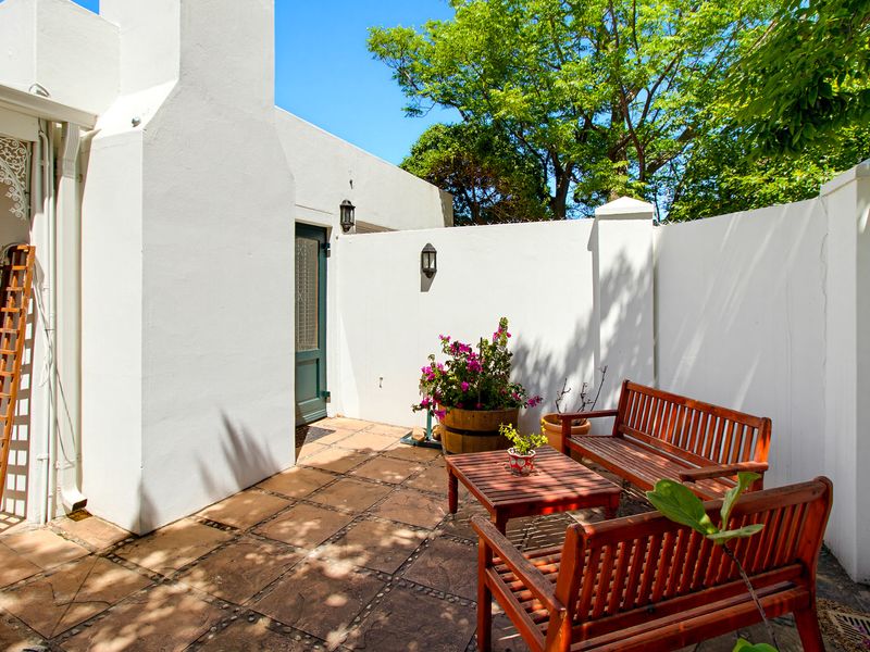 A private, paved outdoor patio area featuring white boundary walls, exterior lighting, and decorative architectural detailing, perfect for quiet relaxation.