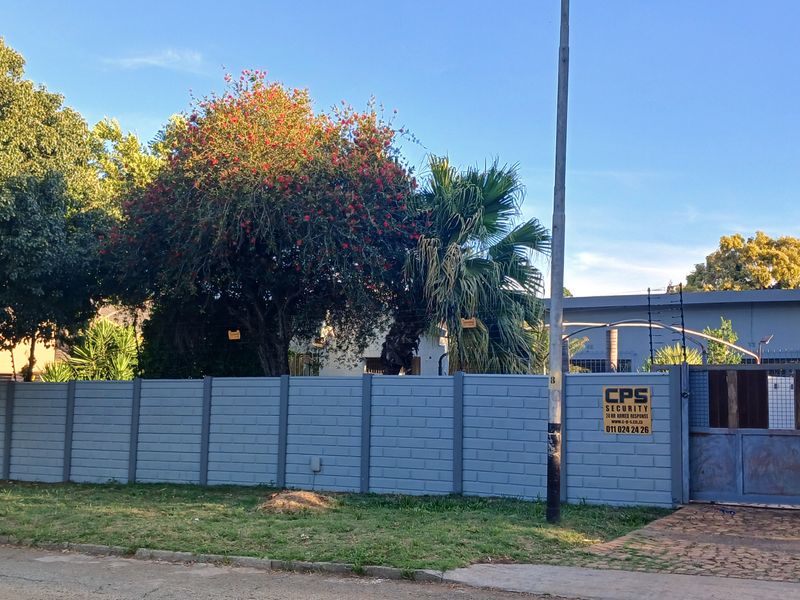 Front view of the property featuring a secure precast concrete boundary wall, sliding driveway gate, and integrated electric fencing.