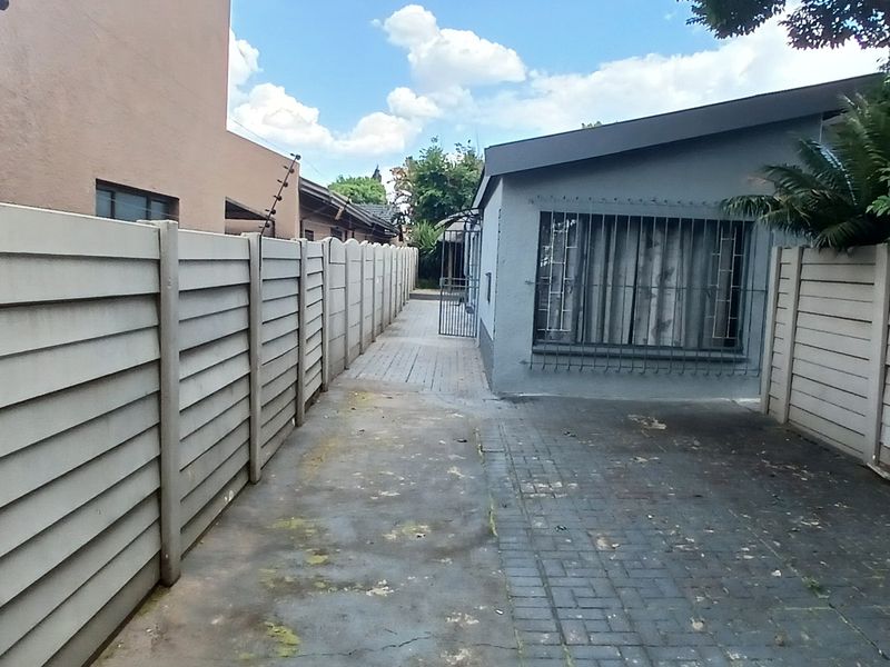 A narrow rear exterior area featuring precast concrete boundary walls with electric fencing and a paved driveway leading to a side entrance.