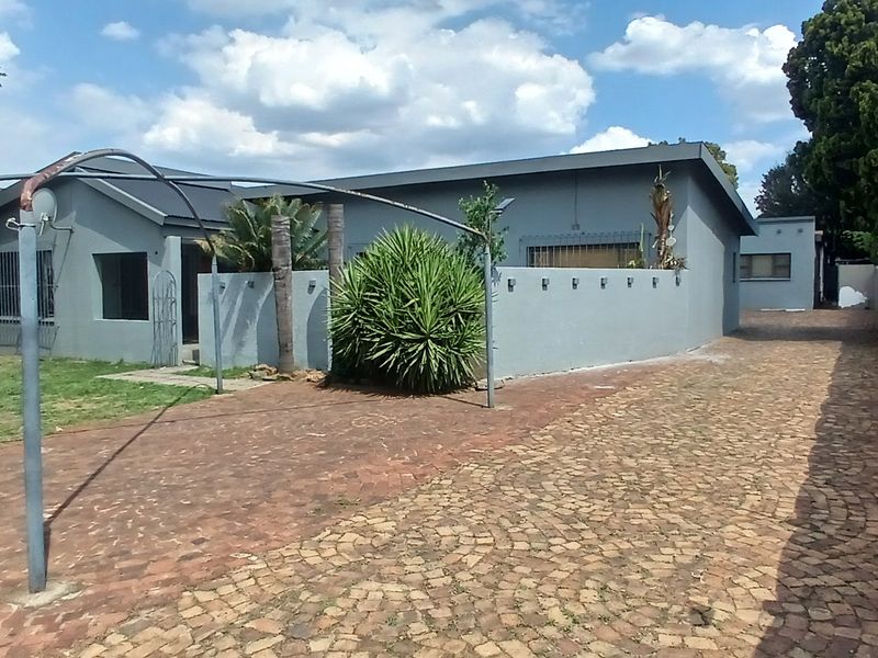 Front exterior view of the house featuring a paved driveway, precast boundary wall, and security bars on windows.