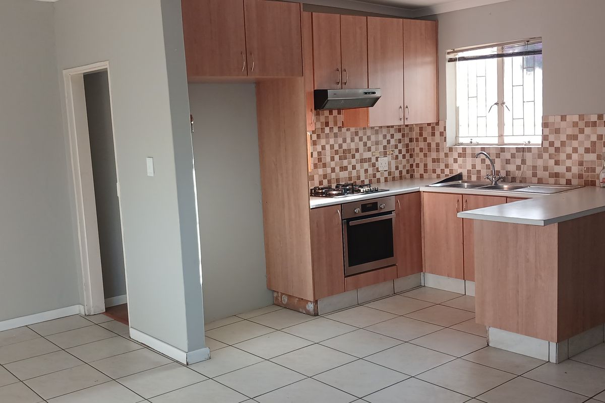 An open-plan kitchen featuring wood-finish cabinetry, built-in oven, gas hob, tiled backsplash, and a breakfast counter, with tiled flooring throughout.