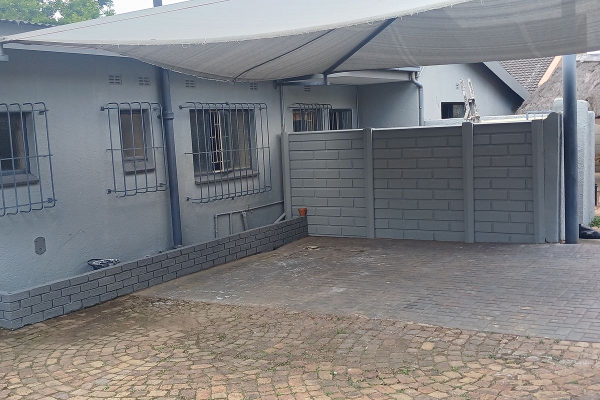 Rear exterior area featuring a paved driveway, shade sail covering, and a brick planter box against the building facade.