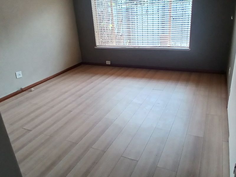 An empty bedroom featuring light-toned laminate flooring, built-in cupboards, and venetian blinds on the window.