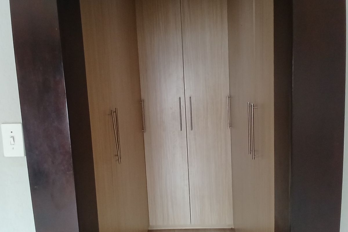 A view of built-in wooden cupboards with modern handles, integrated into a bedroom wall alcove.