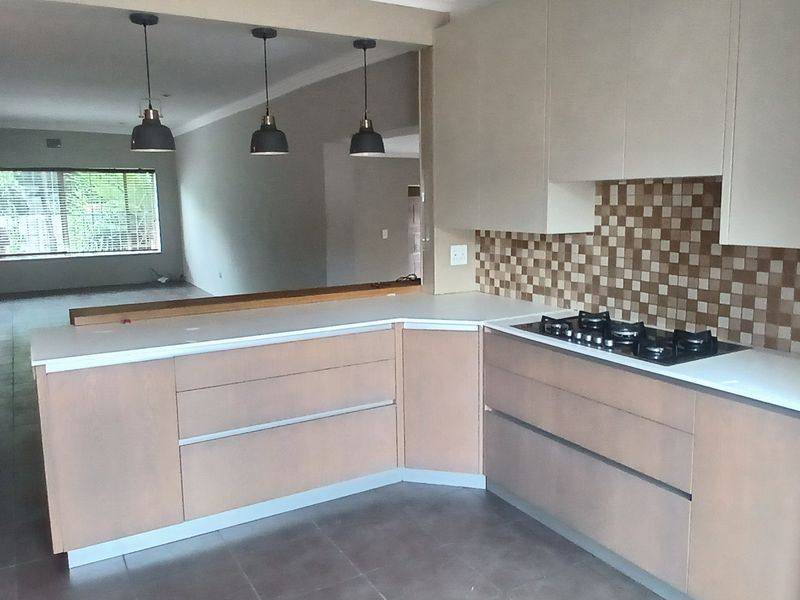 An open-plan kitchen featuring modern cabinetry, a gas hob, built-in oven, and a breakfast bar, flowing into a spacious living area with tiled floors.