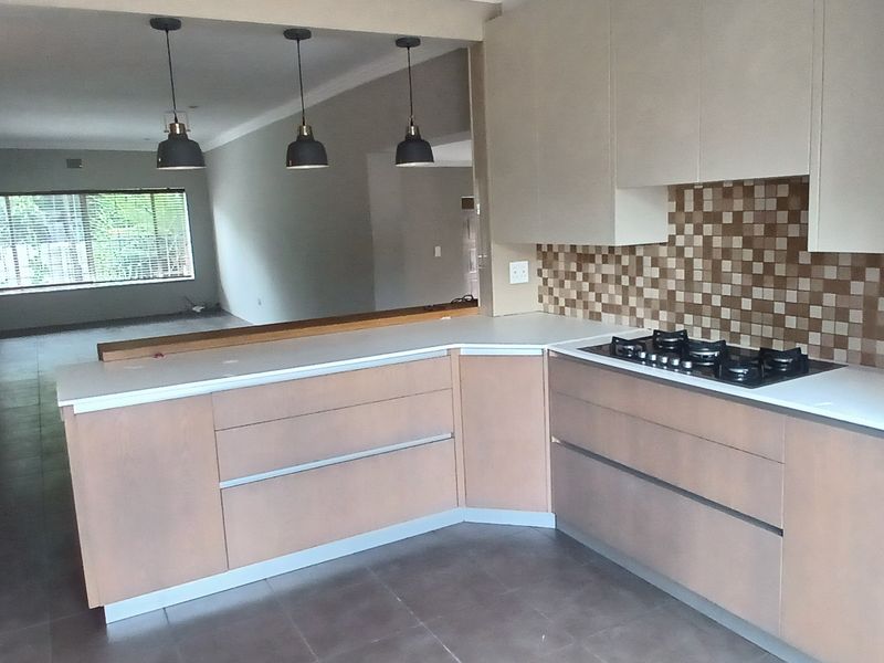 An open-plan kitchen featuring modern cabinetry, a gas hob, built-in oven, and a mosaic tile backsplash, flowing into a spacious living area.