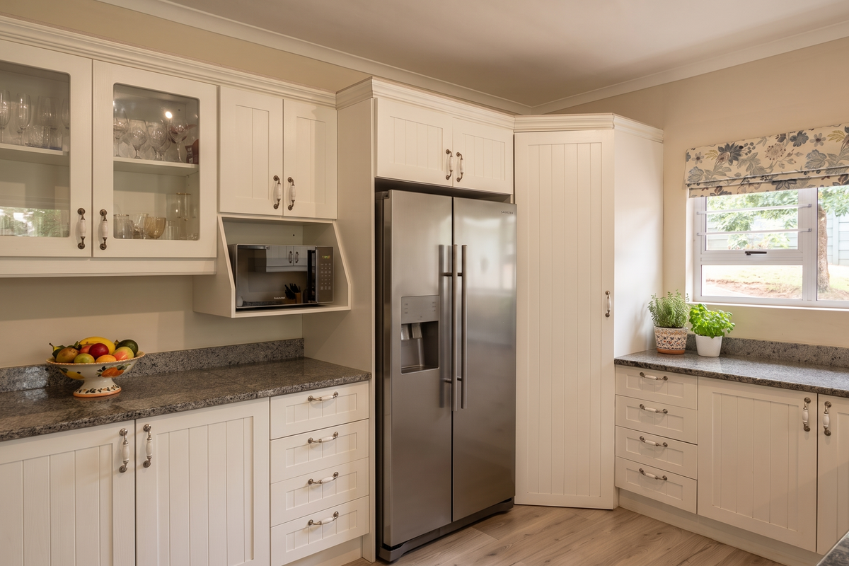 A well-maintained kitchen featuring white shaker-style cabinetry, granite countertops, and a built-in microwave, complemented by light wood-look flooring and natural light.