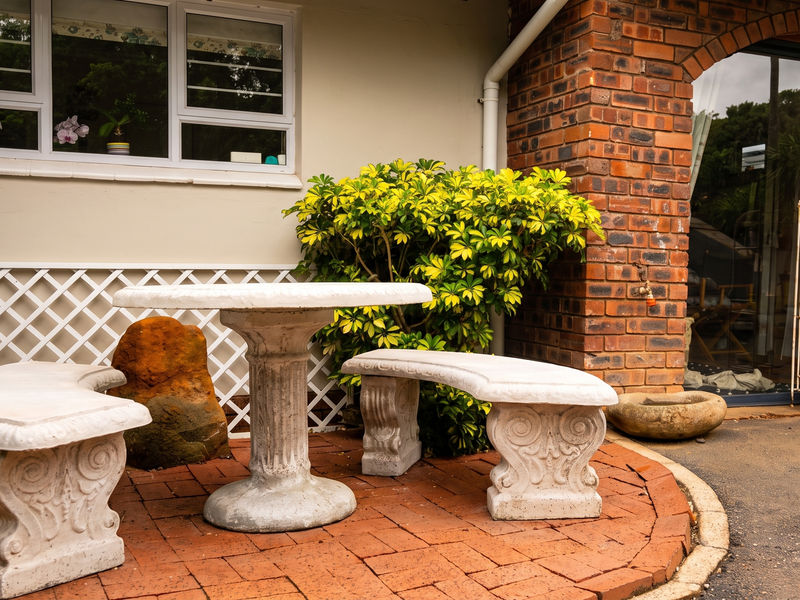 A paved outdoor patio area featuring a brick facade, sliding glass door access, and established garden landscaping.