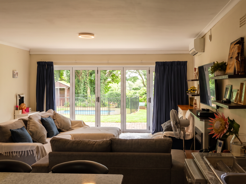 Spacious open-plan living area featuring tiled floors, split-system air conditioning, and large sliding glass doors providing direct access to the rear garden and pool.