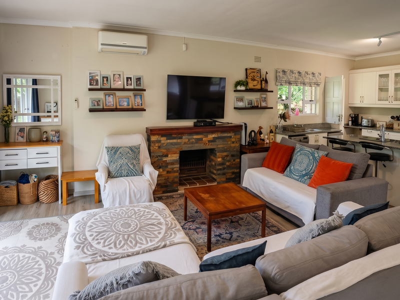 Spacious open-plan living area featuring a stone-clad fireplace, modern kitchen with island, and direct access to the garden through glass sliding doors.