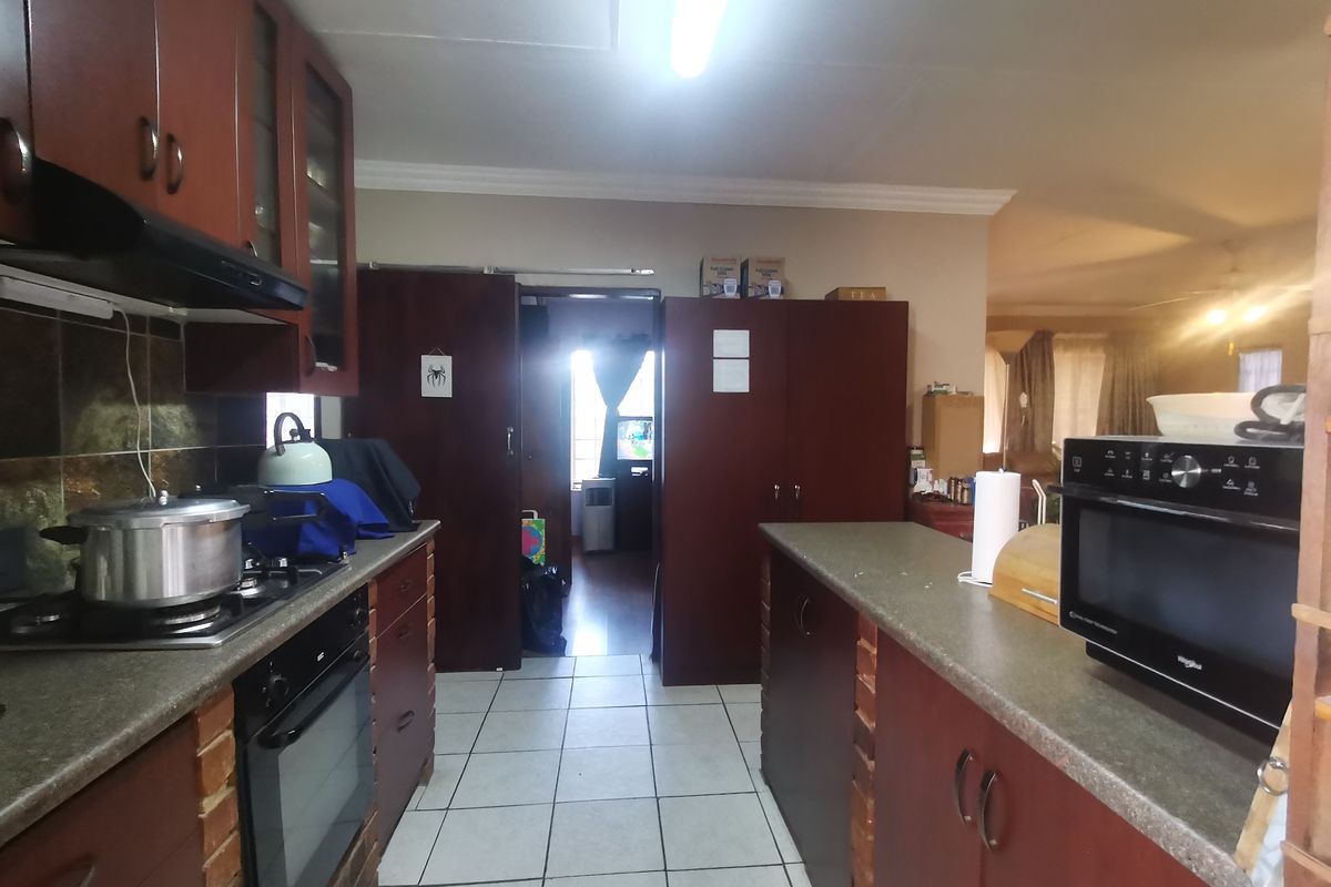 A functional kitchen featuring dark wood cabinetry, stone countertops, built-in oven and hob, and tiled flooring, offering a practical layout for daily meal preparation.