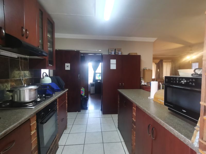 A functional kitchen featuring dark wood cabinetry, stone countertops, built-in oven and hob, and tiled flooring, offering a practical layout for daily meal preparation.