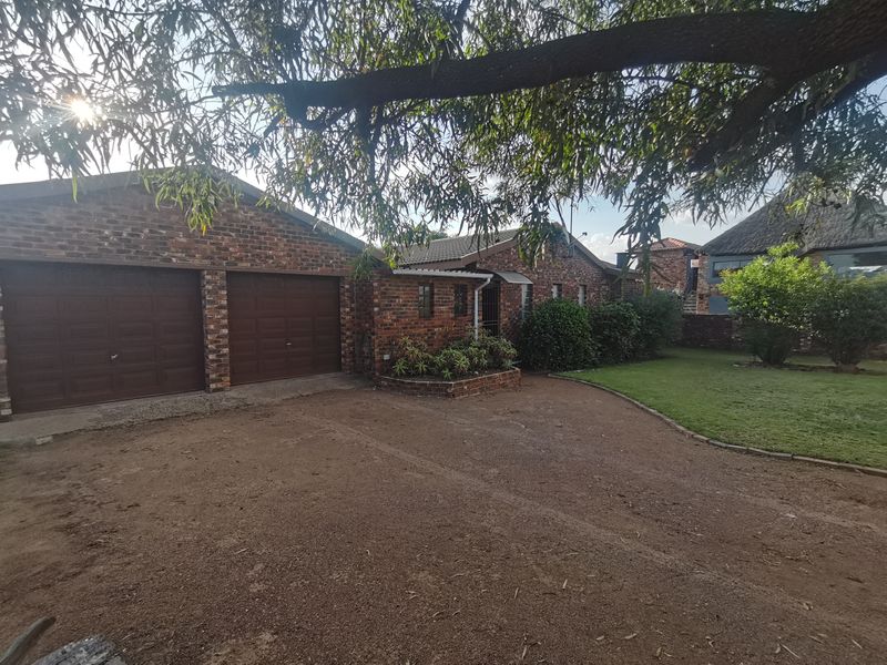 Front view of a facebrick house featuring a double garage, established garden, and a large driveway area.