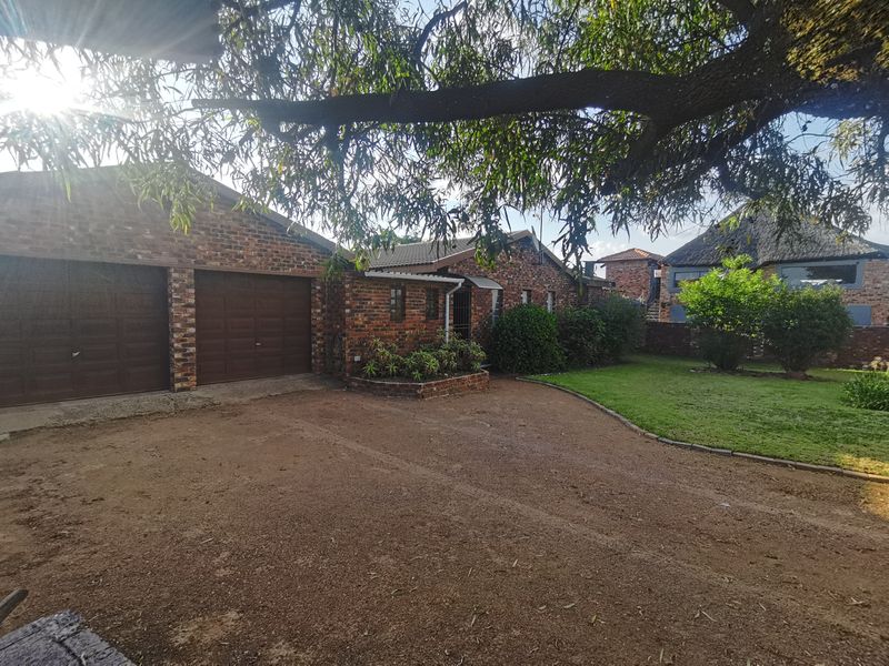 Front exterior view of a brick house featuring a double garage, paved driveway, and established garden area.