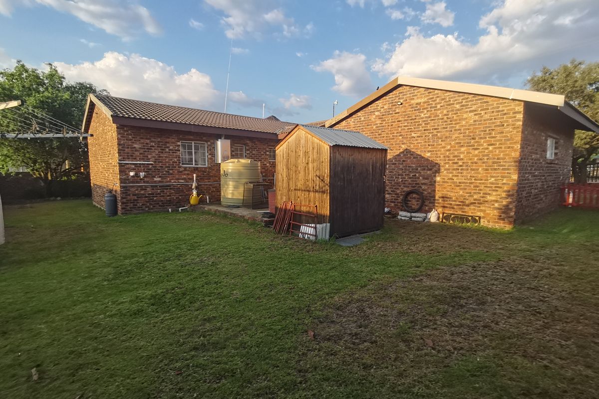 Rear view of the property featuring a face brick exterior, a water storage tank, and a spacious garden area with a timber shed.