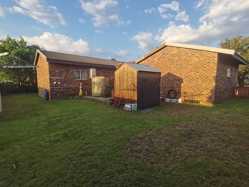 Rear view of the property featuring a face brick exterior, a water storage tank, and a spacious garden area with a timber shed.