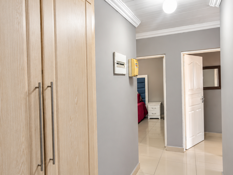A clean, well-maintained hallway featuring light wood-finish built-in cupboards, neutral grey walls, tiled flooring, and crown molding details.