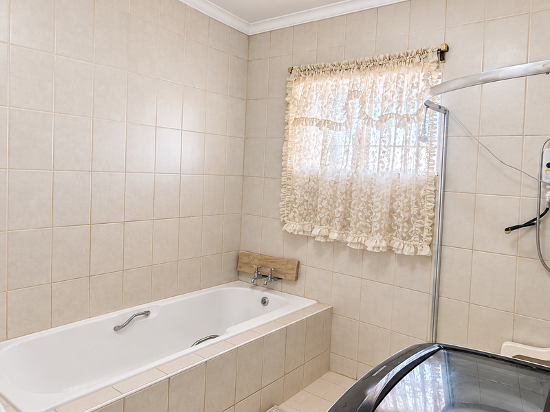 A functional bathroom featuring a built-in bathtub, wall-mounted electric shower unit, and neutral wall tiling throughout.