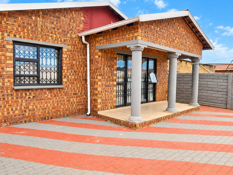 A well-maintained face brick home featuring a covered porch with concrete columns, secure window bars, and a paved driveway.
