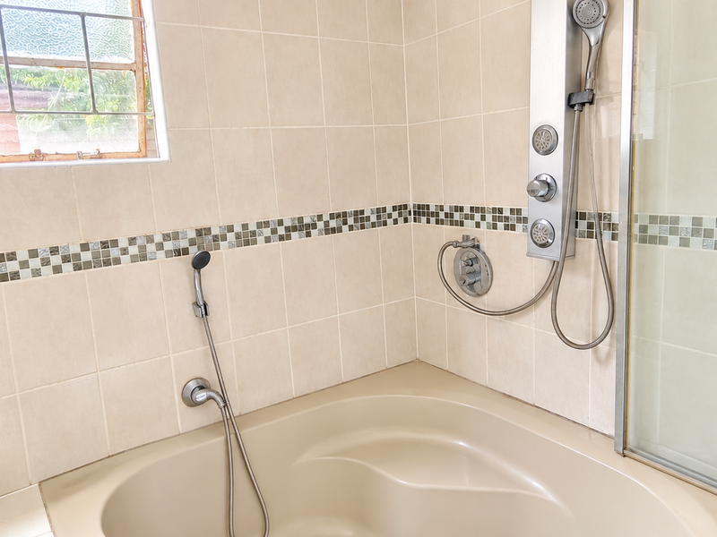 A bathroom featuring a built-in bathtub, a modern shower panel with handheld attachment, and neutral wall tiling with a decorative mosaic border.