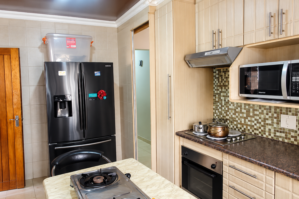 A functional kitchen featuring light wood cabinetry, mosaic tile backsplash, laminate countertops, and integrated appliances including an oven, hob, and microwave.