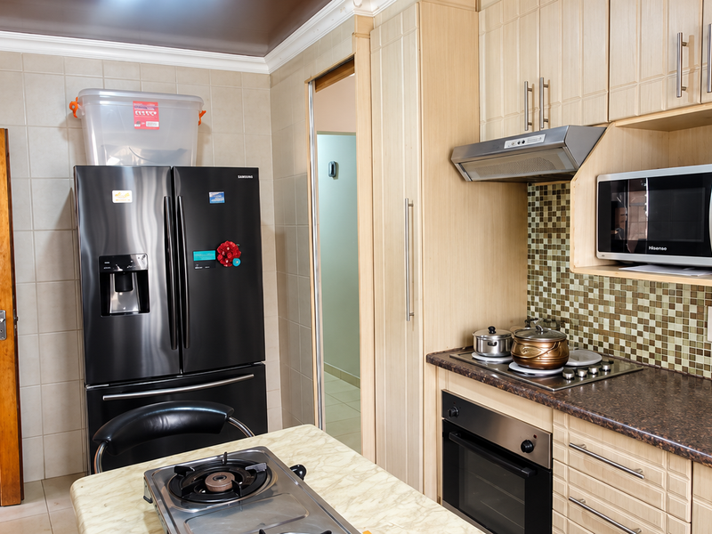 A functional kitchen featuring light wood cabinetry, mosaic tile backsplash, laminate countertops, and integrated appliances including an oven, hob, and microwave.