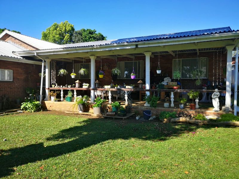 A spacious covered patio area featuring brick construction, classic support columns, and a balustrade, overlooking a well-maintained garden.