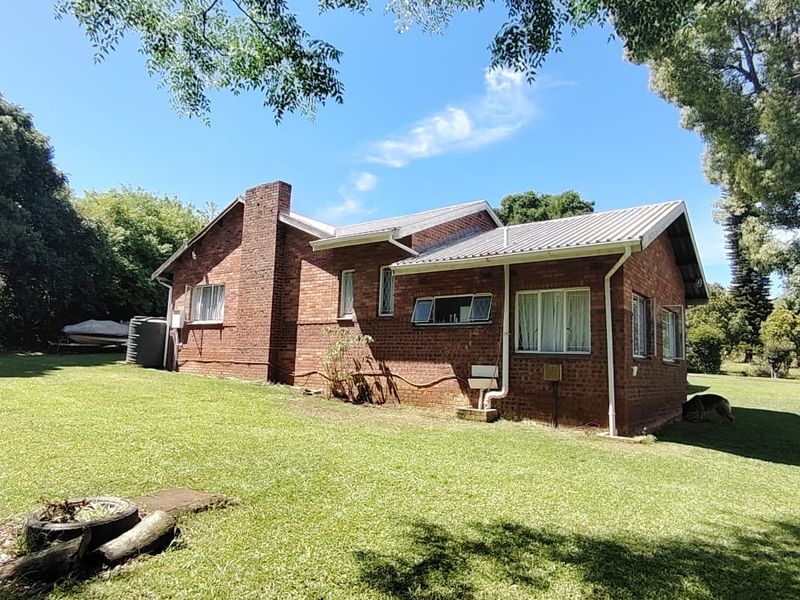 Rear view of a traditional brick house featuring a chimney, corrugated metal roof, and established garden surroundings.