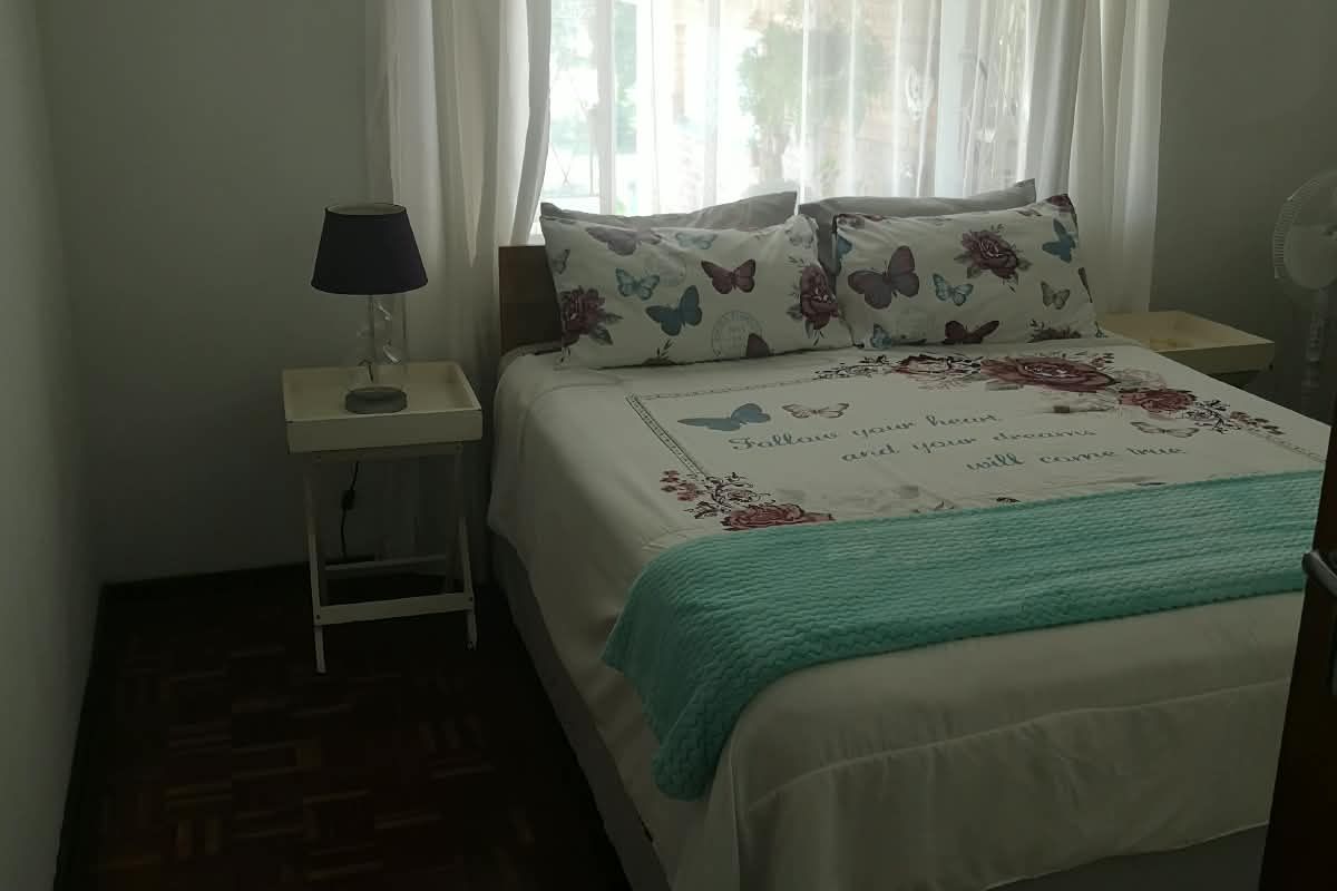 A cozy bedroom featuring classic parquet flooring and natural light through a window with curtain rails.