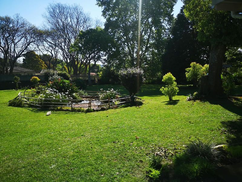 A spacious, well-maintained garden featuring a manicured lawn, mature trees, and a decorative fenced garden bed.