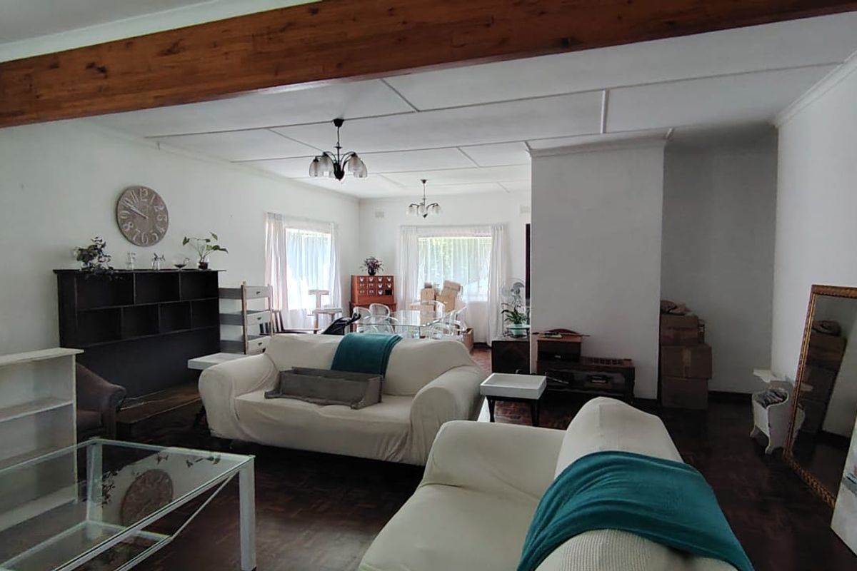 Spacious living area featuring classic parquet flooring, a prominent exposed timber ceiling beam, and large windows allowing for natural light.