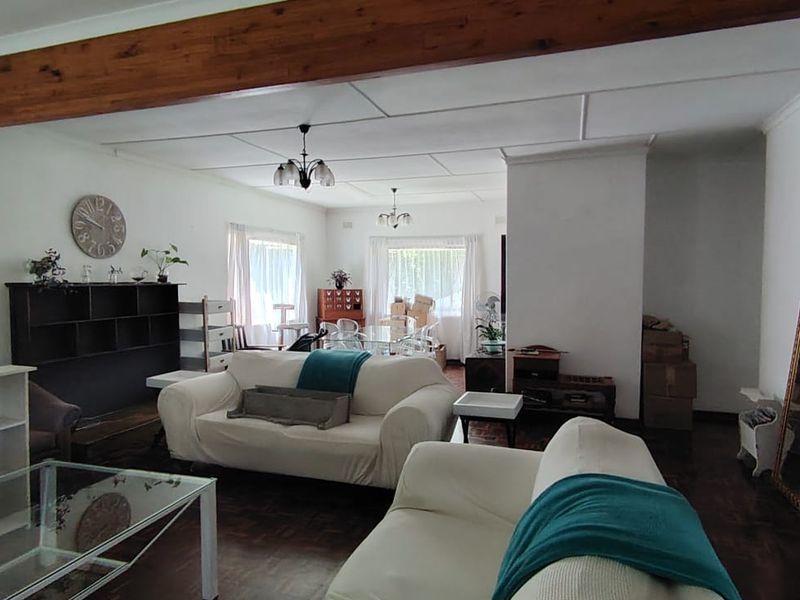 Spacious living area featuring classic parquet flooring, a prominent exposed timber ceiling beam, and large windows allowing for natural light.